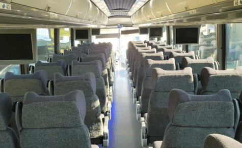 The image shows rows of premium gray bus seating with overhead TV monitors, highlighting group travel comfort for the World Cup 2026