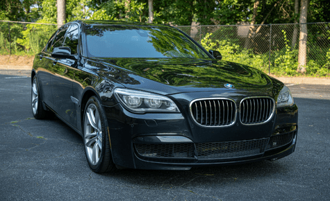 A front-angle shot of a black BMW luxury sedan parked in a lot with green trees in the background